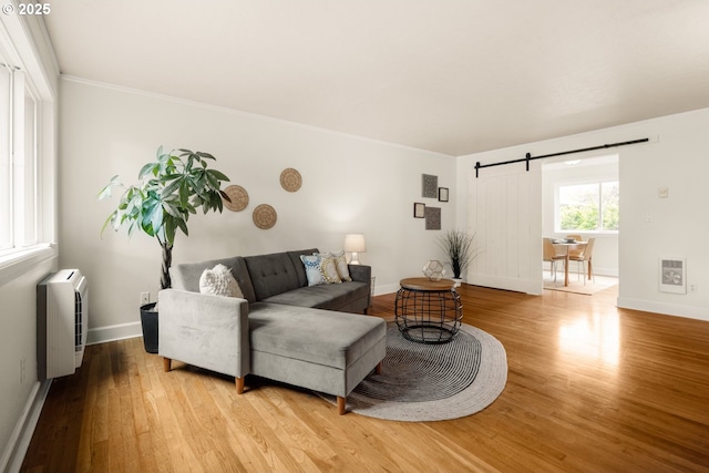 living area with a barn door, wood finished floors, baseboards, and crown molding