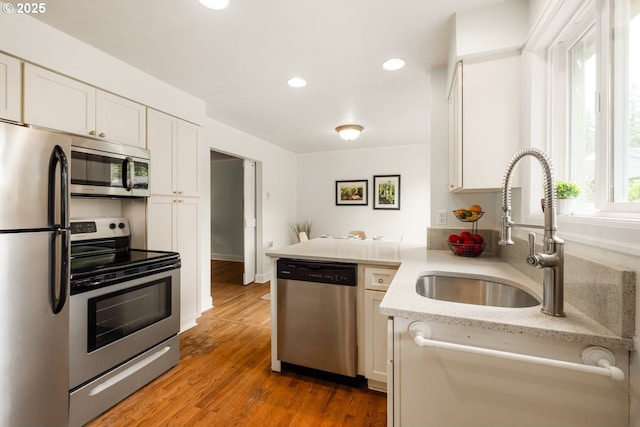 kitchen with stainless steel appliances, a sink, white cabinetry, a peninsula, and recessed lighting