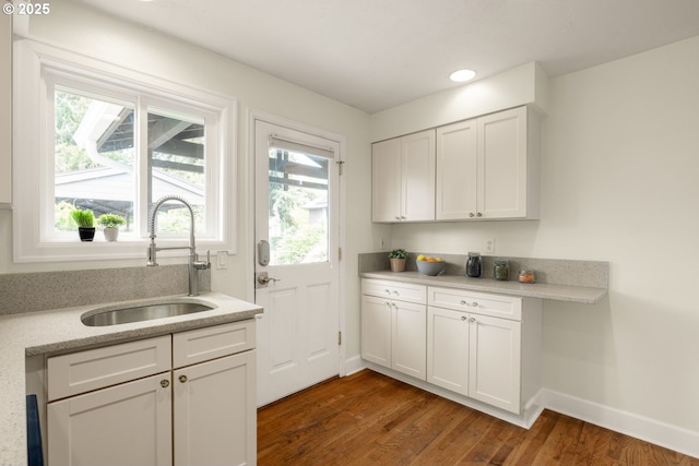 kitchen with a sink, wood finished floors, light countertops, baseboards, and white cabinets