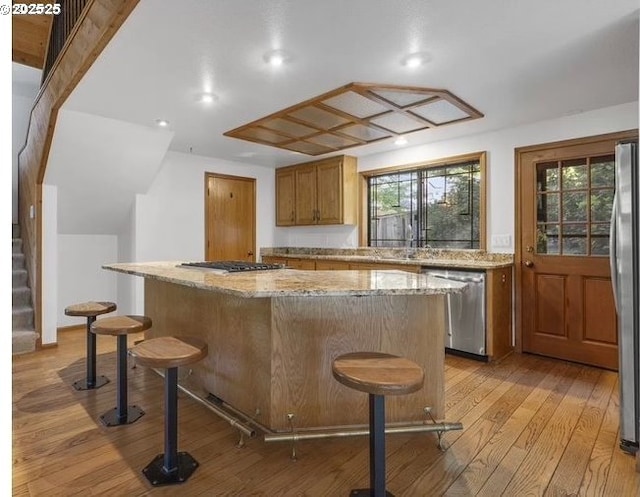 2703 Moon Mountain Dr, Eugene, OR 97403 - kitchen with stainless steel appliances, a center island, light wood-type flooring, a kitchen bar, and light stone countertops
