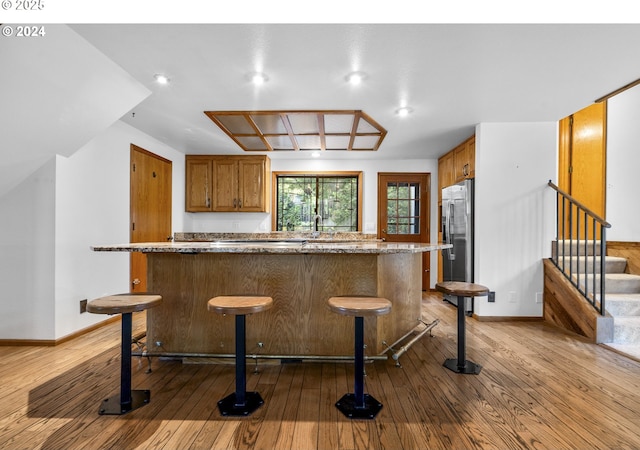2703 Moon Mountain Dr, Eugene, OR 97403 - kitchen with wood-type flooring, brown cabinets, a breakfast bar area, stainless steel fridge, and a kitchen island