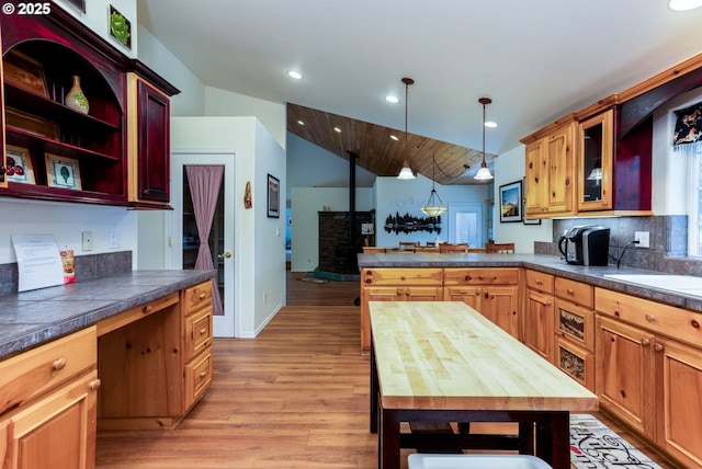 kitchen featuring kitchen peninsula, light hardwood / wood-style flooring, decorative light fixtures, vaulted ceiling, and wooden counters