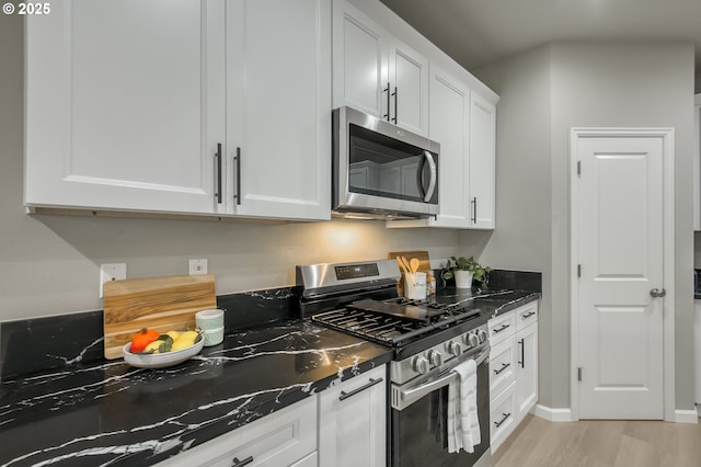 kitchen featuring baseboards, dark stone counters, light wood-style flooring, stainless steel appliances, and white cabinetry