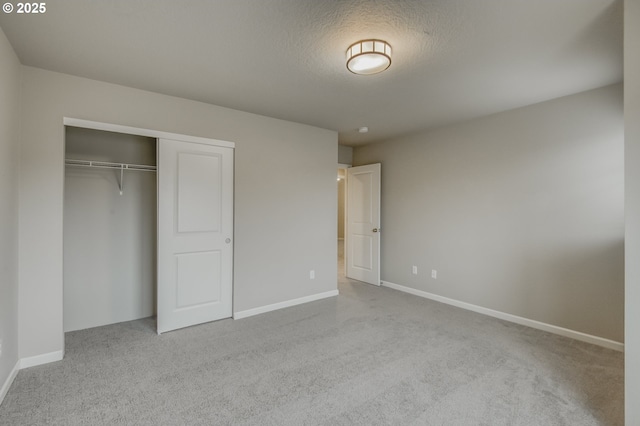 unfurnished bedroom featuring light carpet, a closet, a textured ceiling, and baseboards