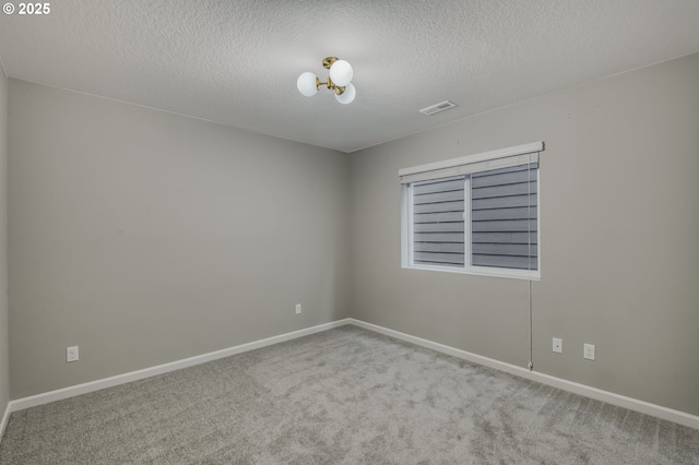 spare room featuring baseboards, a textured ceiling, visible vents, and light colored carpet