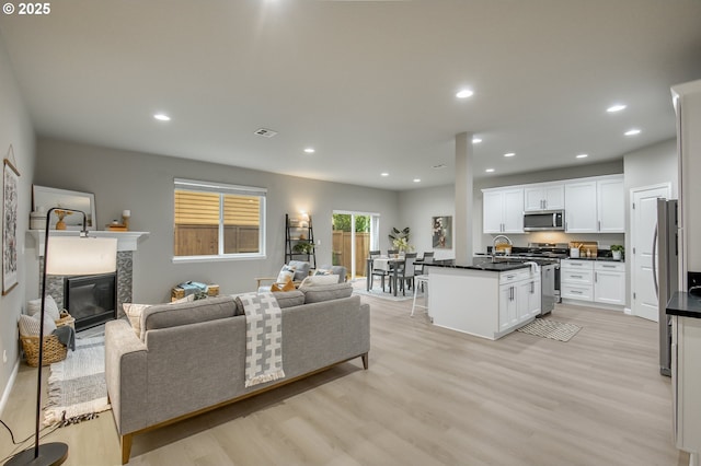 living area featuring light wood-style floors, a glass covered fireplace, visible vents, and recessed lighting