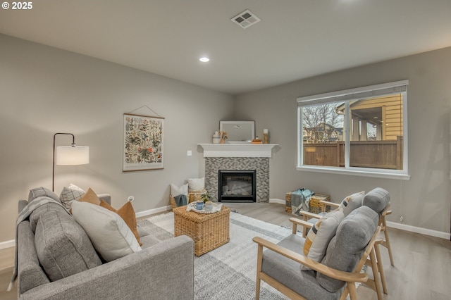 living room featuring light wood-type flooring, baseboards, visible vents, and a tiled fireplace