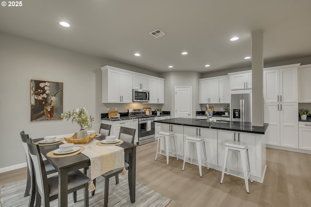 kitchen featuring a center island with sink, dark countertops, visible vents, appliances with stainless steel finishes, and white cabinets