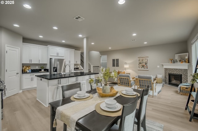 dining room featuring light wood-style flooring, a tiled fireplace, visible vents, and recessed lighting