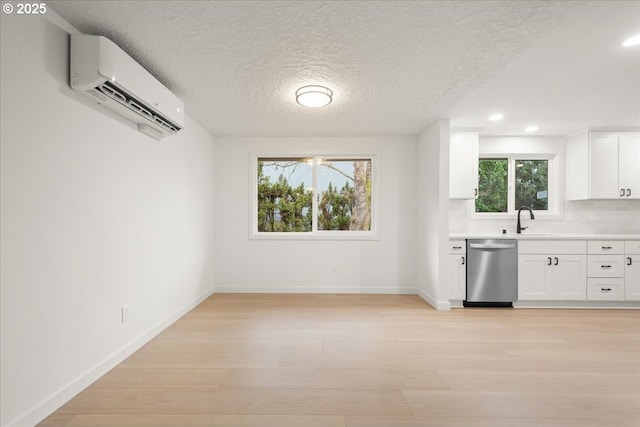 kitchen with dishwasher, light countertops, an AC wall unit, light wood-type flooring, and a sink