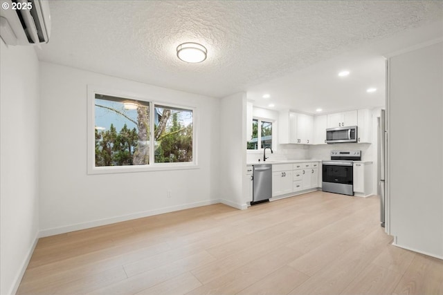 kitchen with light wood finished floors, light countertops, a wall mounted AC, appliances with stainless steel finishes, and white cabinets