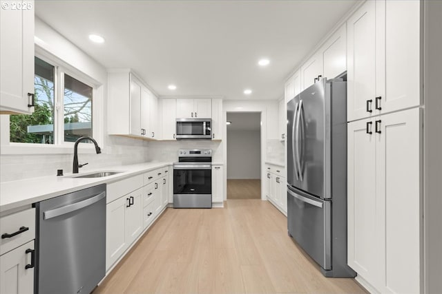 kitchen with stainless steel appliances, light wood-style flooring, decorative backsplash, white cabinets, and a sink