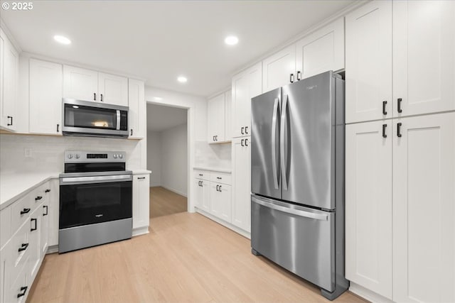 kitchen featuring white cabinetry, light countertops, appliances with stainless steel finishes, light wood-type flooring, and backsplash