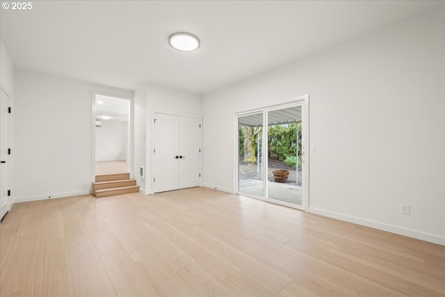 empty room featuring light wood finished floors, baseboards, and stairway