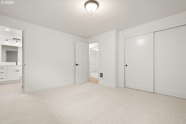 unfurnished bedroom featuring carpet floors, a closet, baseboards, and ensuite bath