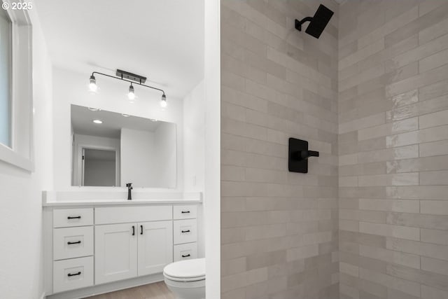 full bathroom featuring toilet, wood finished floors, tiled shower, and vanity