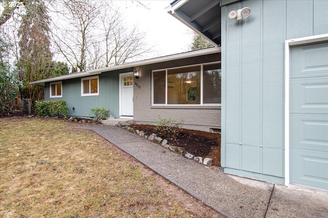 view of exterior entry with a garage, a lawn, and brick siding