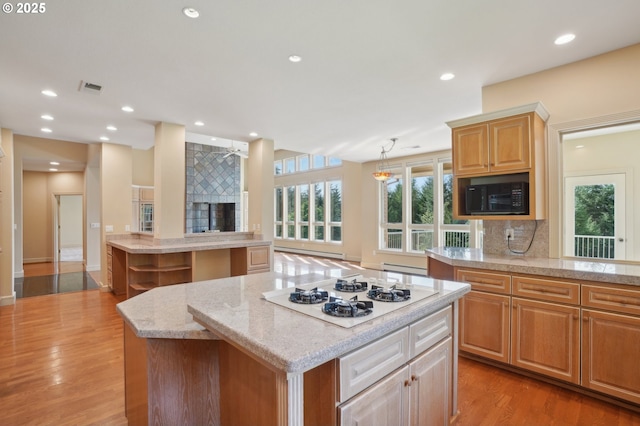 kitchen featuring decorative backsplash, visible vents, black microwave, a center island, and white gas cooktop