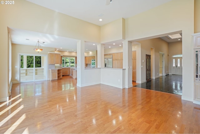 unfurnished living room with a towering ceiling, baseboards, and light wood-type flooring