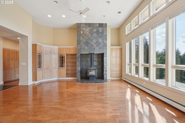 unfurnished living room featuring a high ceiling, a baseboard heating unit, light wood-type flooring, and ceiling fan