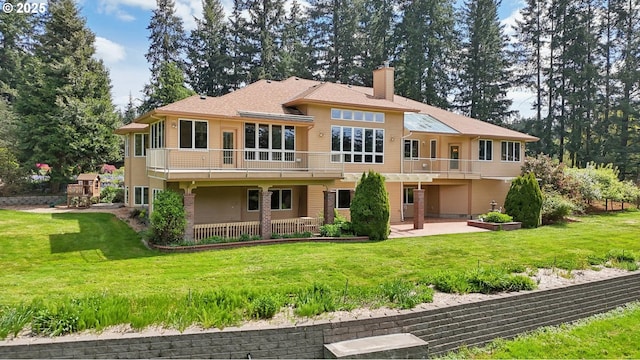 rear view of house with a patio, a chimney, a yard, and a balcony