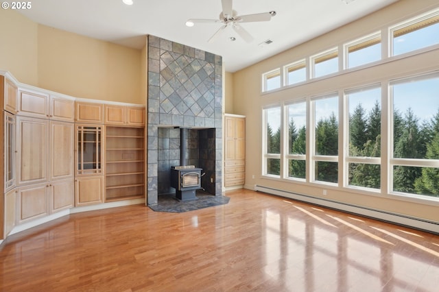 unfurnished living room featuring a ceiling fan, baseboard heating, a wood stove, light wood finished floors, and recessed lighting