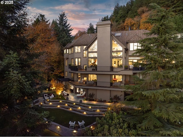 back house at dusk featuring a patio area and a balcony