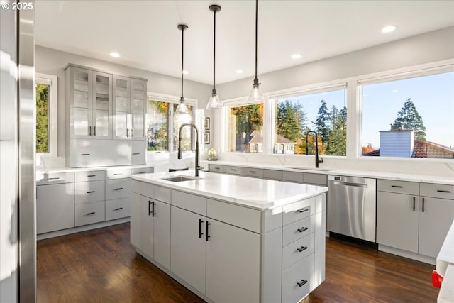 kitchen with hanging light fixtures, an island with sink, sink, and stainless steel dishwasher