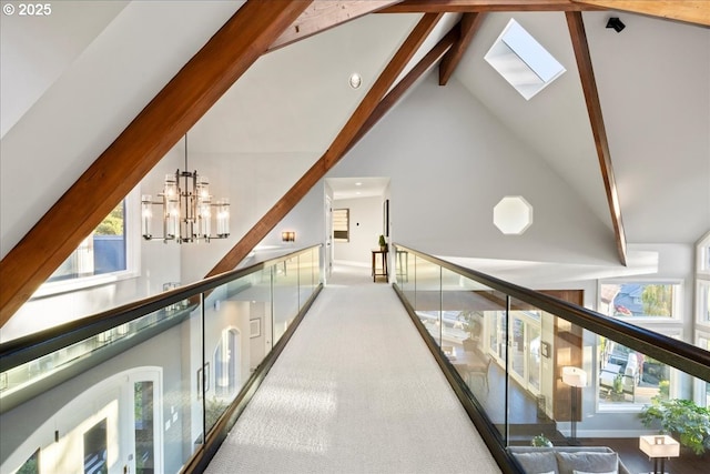 hall featuring an inviting chandelier, a skylight, high vaulted ceiling, light colored carpet, and beam ceiling