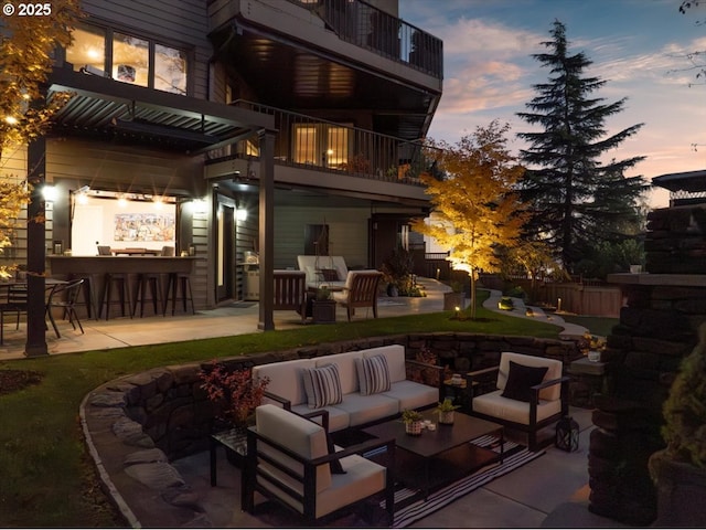 back house at dusk featuring a patio area, an outdoor hangout area, a balcony, and exterior bar