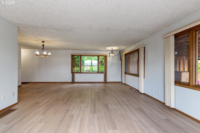 spare room with baseboards, visible vents, light wood-style flooring, a textured ceiling, and a chandelier