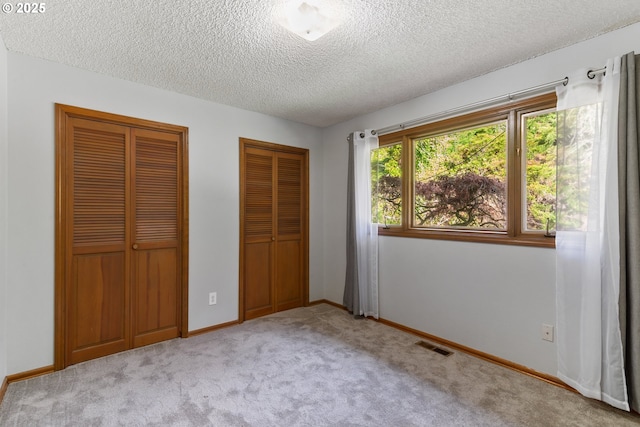 unfurnished bedroom with baseboards, visible vents, carpet, a textured ceiling, and multiple closets