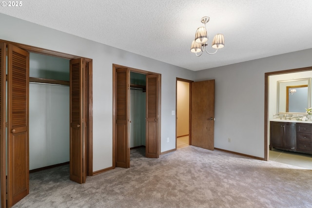 unfurnished bedroom with multiple closets, an inviting chandelier, light carpet, a textured ceiling, and baseboards