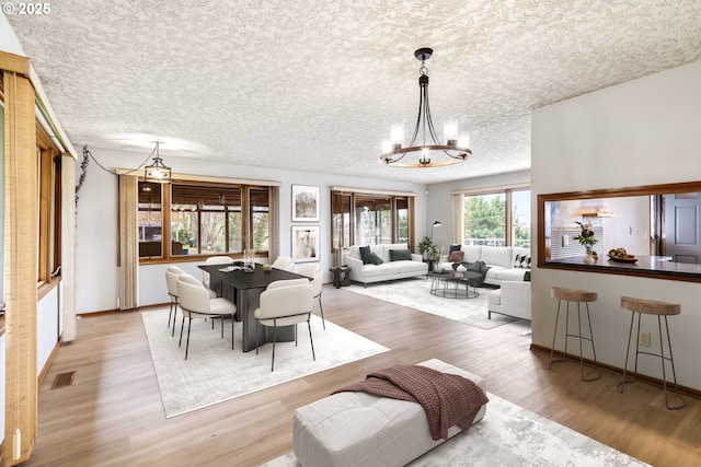 dining room with a textured ceiling, light wood finished floors, visible vents, and a notable chandelier