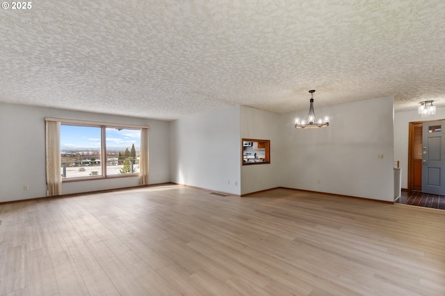 spare room with a chandelier, a textured ceiling, wood finished floors, visible vents, and baseboards