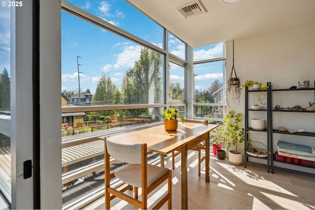 sunroom / solarium with a wall of windows, plenty of natural light, wood finished floors, and visible vents