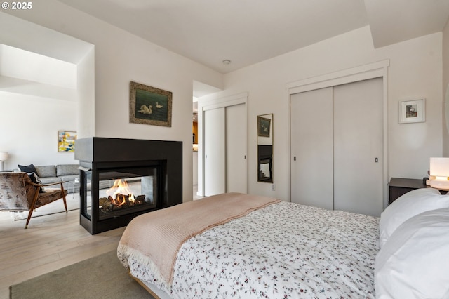 bedroom featuring two closets, wood finished floors, and a multi sided fireplace