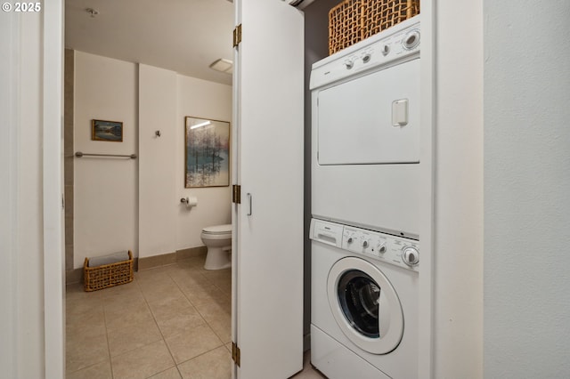 clothes washing area featuring stacked washer / drying machine, laundry area, baseboards, and light tile patterned floors