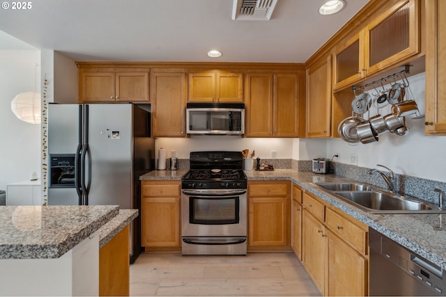 kitchen with light wood finished floors, a sink, visible vents, glass insert cabinets, and appliances with stainless steel finishes