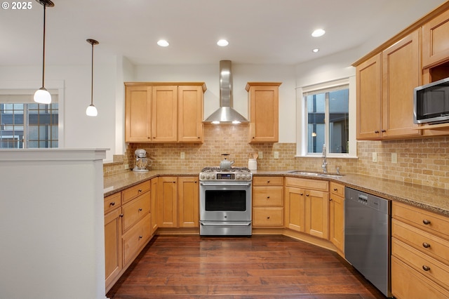 kitchen featuring pendant lighting, wall chimney range hood, sink, stainless steel appliances, and light stone countertops