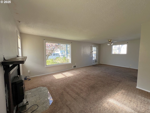 1042 Fir Ave, Reedsport, OR 97467 - unfurnished living room with ceiling fan, a textured ceiling, carpet flooring, and a wood stove