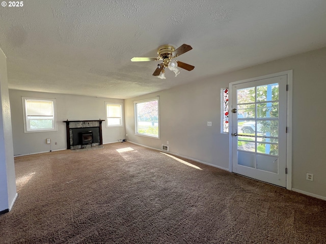 1042 Fir Ave, Reedsport, OR 97467 - unfurnished living room with a textured ceiling, plenty of natural light, ceiling fan, carpet flooring, and a fireplace with flush hearth