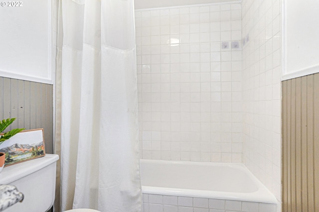 bathroom featuring toilet, a wainscoted wall, and tiled shower / bath combo