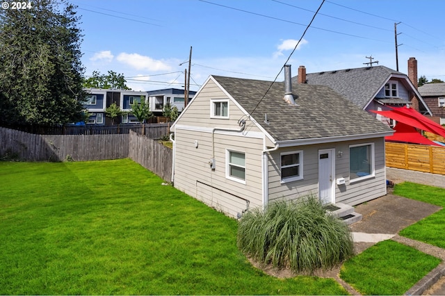 rear view of house featuring a yard, a shingled roof, a chimney, and a fenced backyard