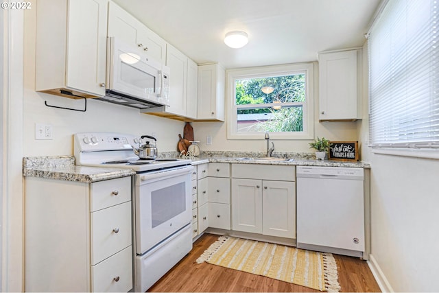 kitchen with white appliances, a sink, white cabinetry, light wood-type flooring, and light stone countertops