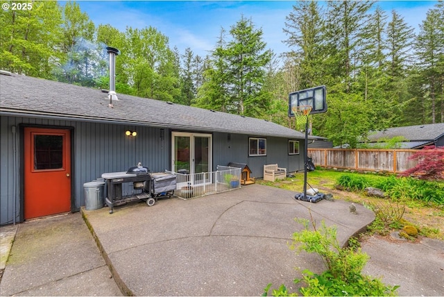 rear view of house featuring a patio area, fence, and a shingled roof