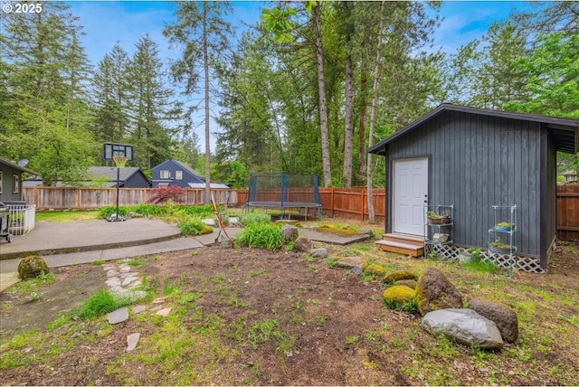fenced backyard featuring a trampoline, a patio area, and an outbuilding