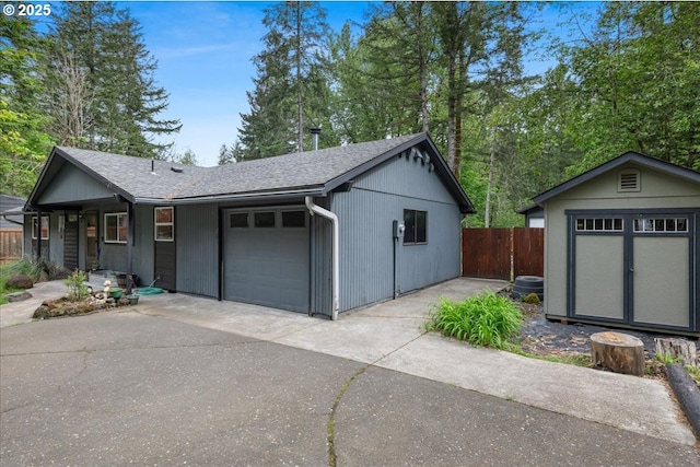 garage featuring fence, concrete driveway, and a storage shed