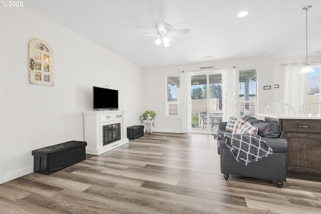 living area with baseboards, a glass covered fireplace, ceiling fan, wood finished floors, and recessed lighting