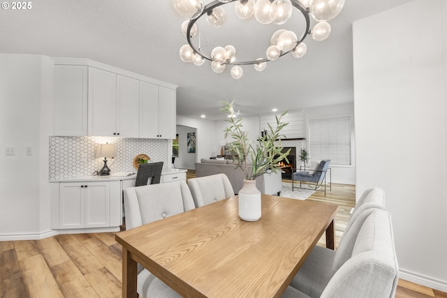 dining area with a chandelier, light wood-style flooring, baseboards, a lit fireplace, and recessed lighting